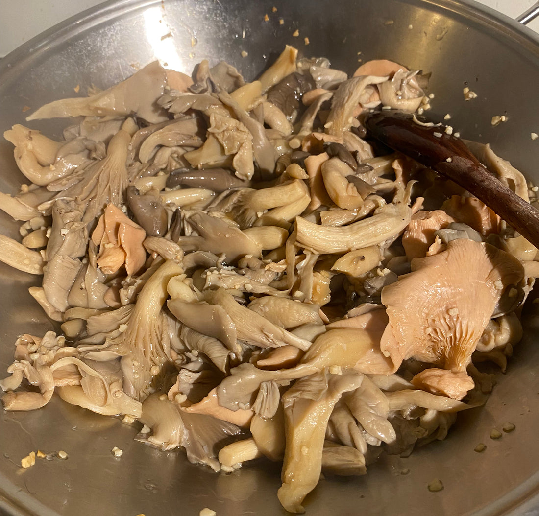 Oyster mushrooms cooking in a pan with garlic and a small amount of water, partially cooked before finishing and browning.